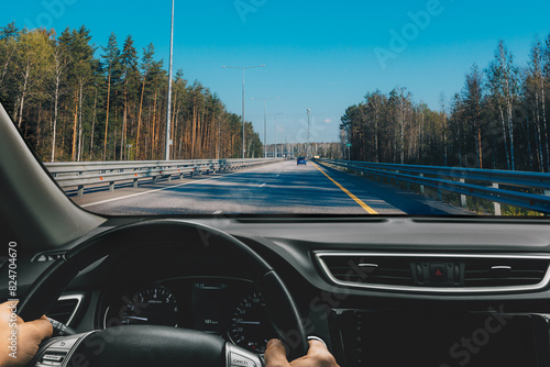Obraz na płótnie Hands of car driver on steering wheel. Man driving car on asphalt highway road in summer Finland. w salonie