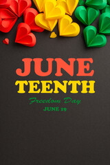 Vibrant vertical display of red, yellow, and green paper hearts representing unity and love on a dark backdrop, creating a thematic visual for Juneteenth
