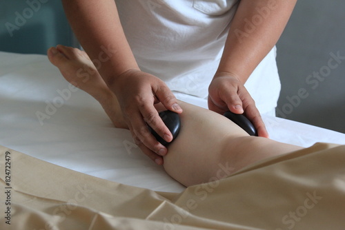 Close-up cut of professional masseuse doing hot stone massage service to her female customer, relaxation, spa treatment, wellness, resort, hotel, leisure.