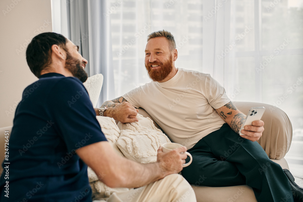 Two men in casual clothes, a happy gay couple, sit on a couch in a modern living room, engaging in a lively conversation. Two men in casual clothes, a happy gay couple, sit on a couch in a modern living room, engaging in a lively conversation.