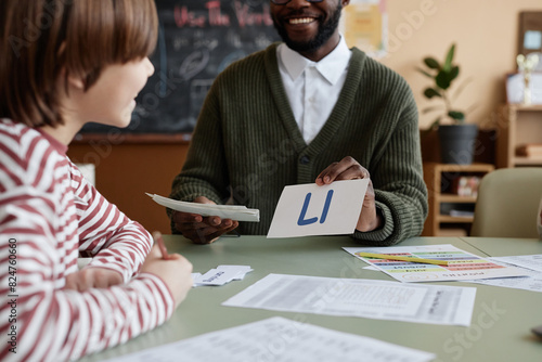 Foto Crop shot of cheerful Black teacher of English sitting at table in classroom sho