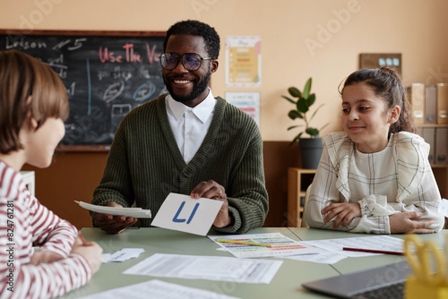 Tableau sur toile Cheerful African American male teacher of English working with group of kids sho