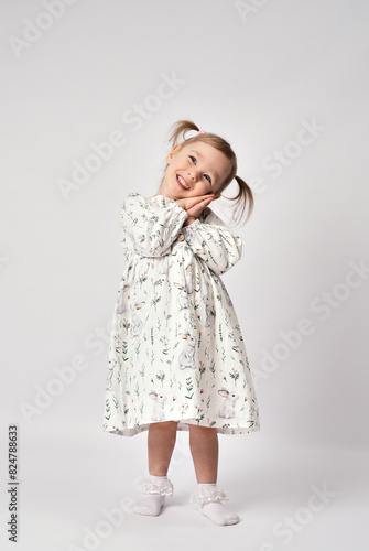 Portrait of cute little girl on a white background. Full length standing and smiling little girl, wearing white dress looking at camera