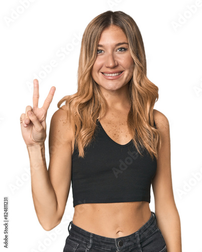 Caucasian blonde woman in studio joyful and carefree showing a peace symbol with fingers.