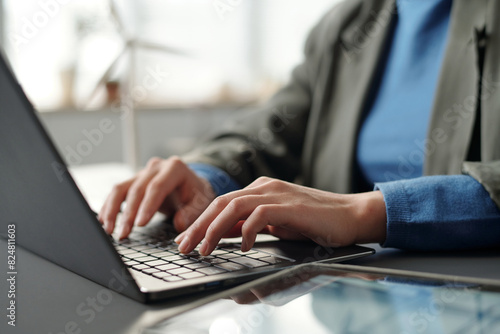 Hands of young unrecognizable businesswoman in smart casualwear touching keys of laptop keyboard during work over new project