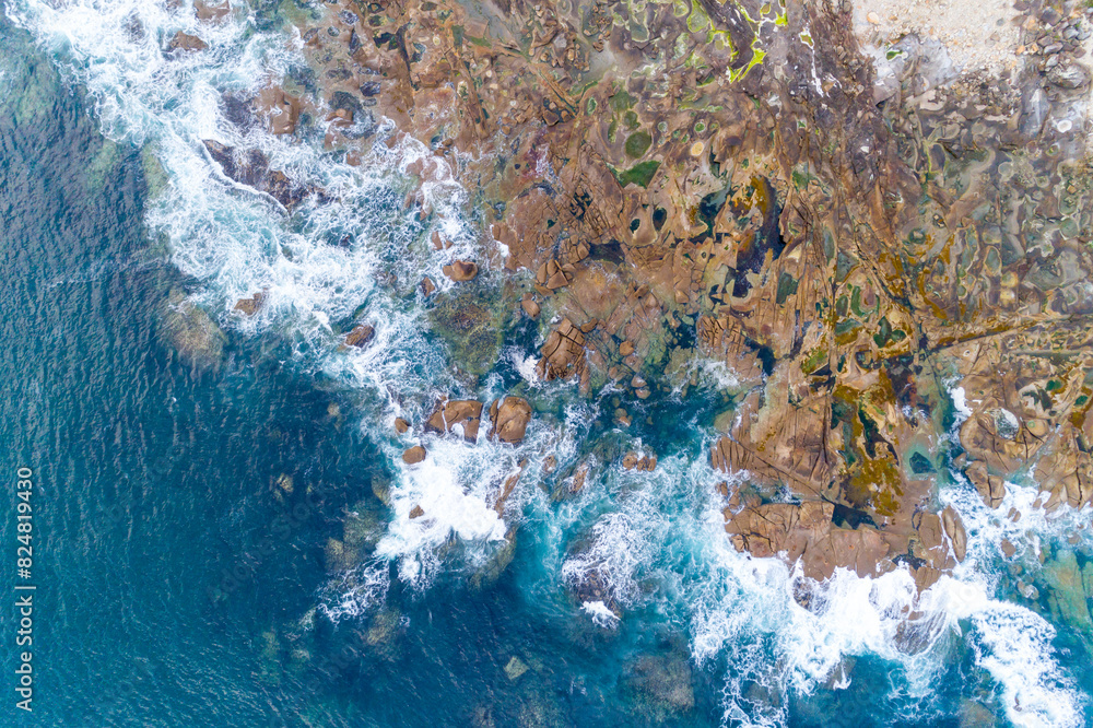 foam of the waves on the shore of a rocky coast, aerial directly above view with drone