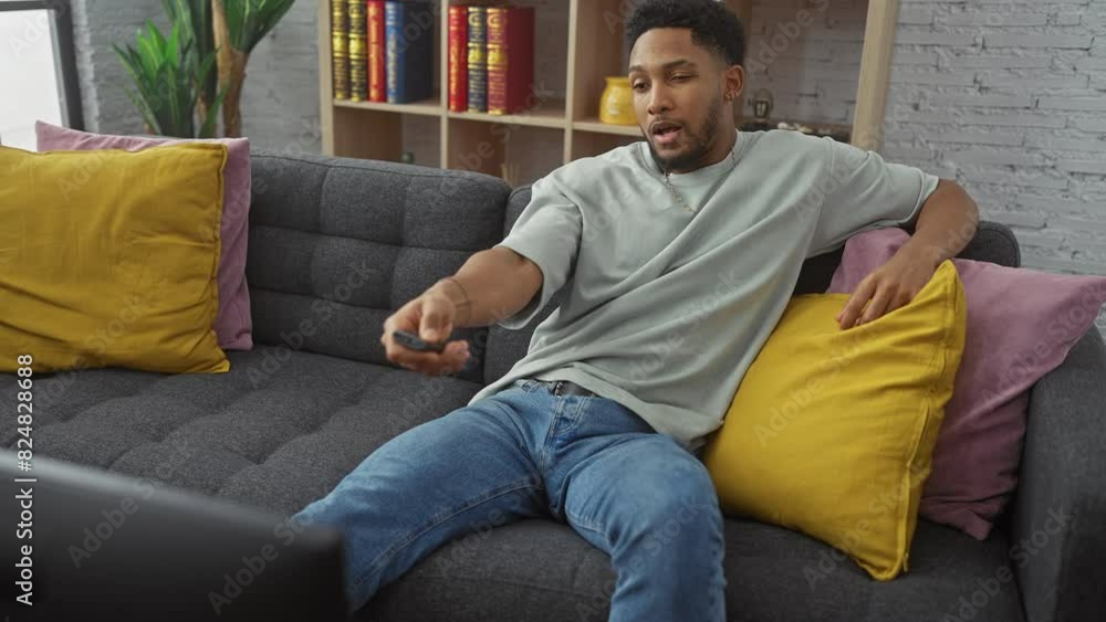 A relaxed african american man switches channels on a remote while lounging on a couch in a cozy living room. A relaxed african american man switches channels on a remote while lounging on a couch in a cozy living room.