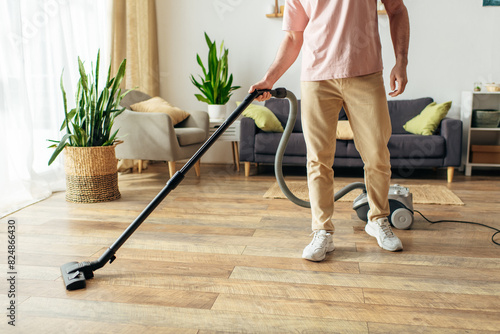 A handsome man in cozy homewear using a vacuum to clean the floor.