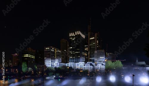 Beleuchtete Skyline einer modernen Metropole bei Nacht mit hell erleuchteten Wolkenkratzern und Spiegelungen auf der Wasseroberfläche eines Flusses