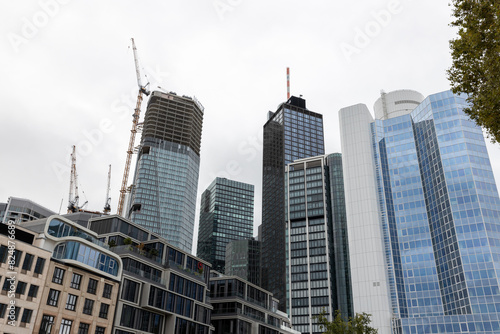 Moderne Hochhäuser und Wolkenkratzer mit Baustellenkränen in einem urbanen Finanzviertel unter bewölktem Himmel
