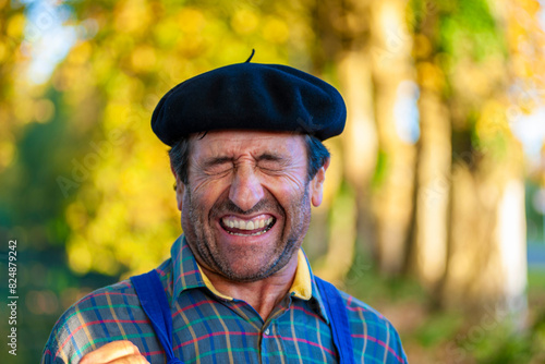 Portrait of a Frenchman, wearing a beret and blue dungarees smiling and gesticulating to camera photo