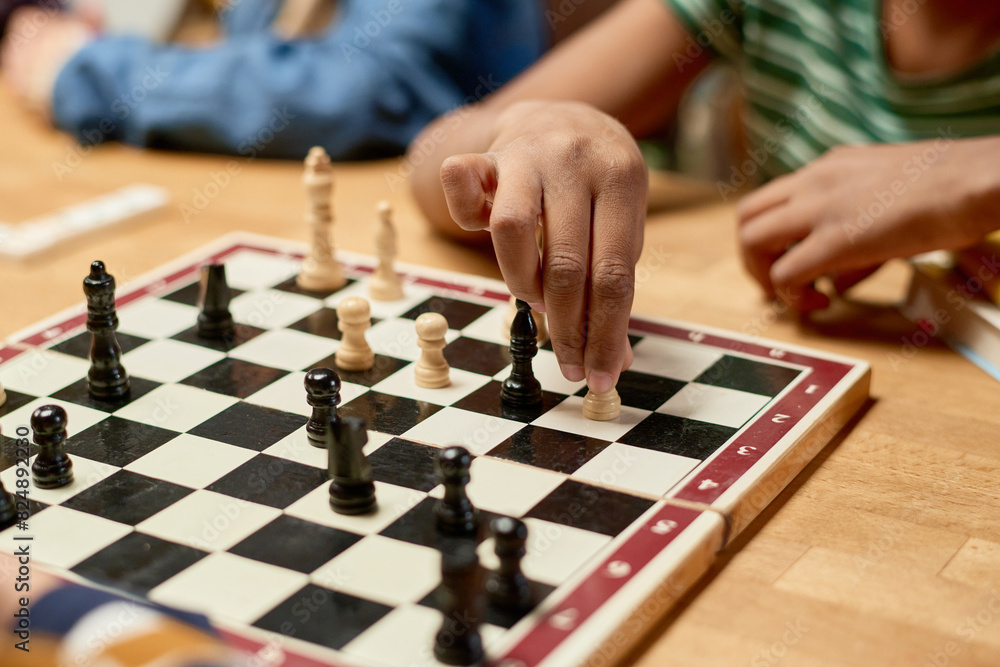 Hand of youthful unrecognizable African American boy moving white pawn or other chess figurine on board while playing tabletop game Hand of youthful unrecognizable African American boy moving white pawn or other chess figurine on board while playing tabletop game