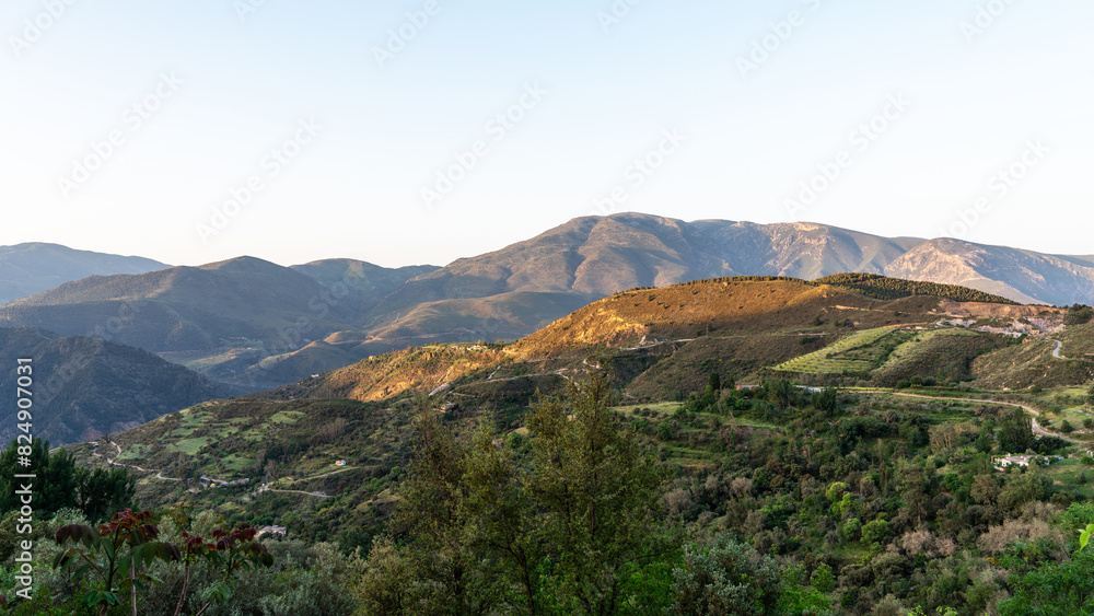 tranquil landscape at golden hour, with rolling hills and mountains bathed in soft sunlight. A tapestry of greenery and cultivated fields is interspersed with winding roads and sparse buildings. tranquil landscape at golden hour, with rolling hills and mountains bathed in soft sunlight. A tapestry of greenery and cultivated fields is interspersed with winding roads and sparse buildings.
