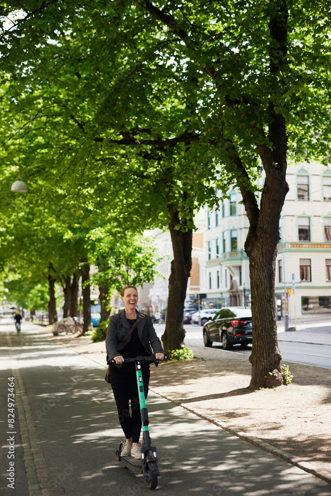 Happy businesswoman riding electric push scooter on footpath