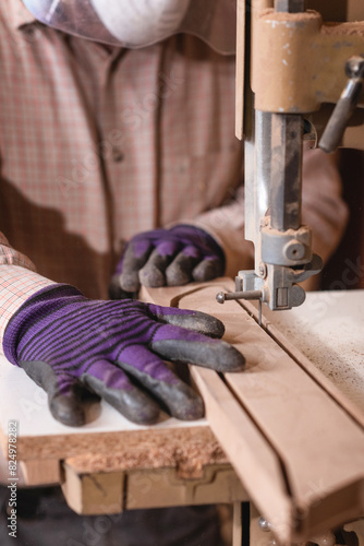 Worker in the carpentry workshop cuts the wooden board using band saw © Microgen