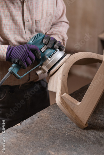Hands of a carpenter treats wooden chair with circular grinding machine