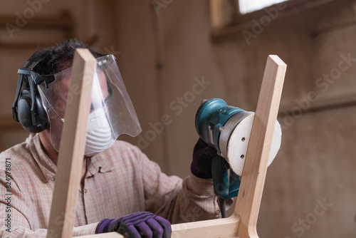 Woodworker grinds the wooden chair with grinding machine in furniture factory