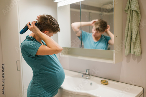 Pregnant woman trimming hair in front of mirror at bathroom photo
