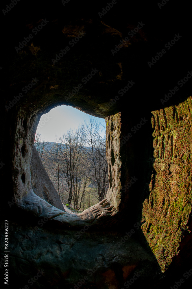 A stone wall with a dark hole, an exit from the cave into the natural environment.
