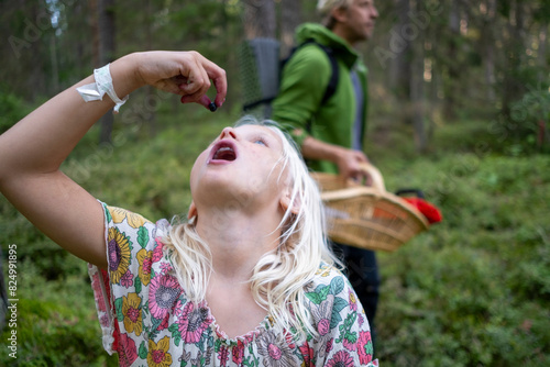 Girl eating berry with father in background at forest photo
