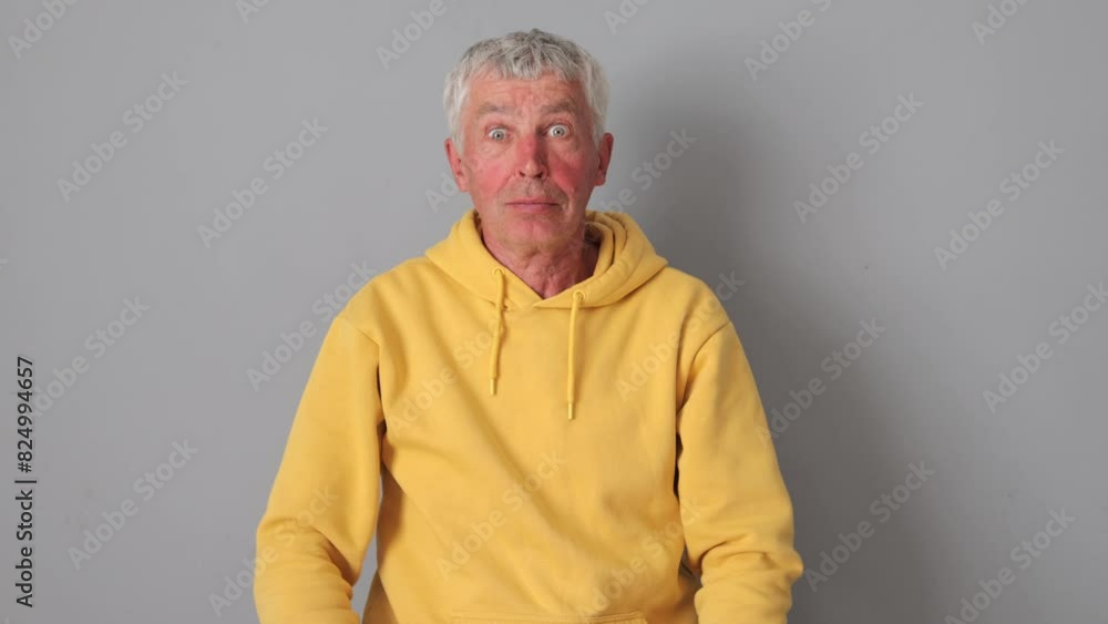 Surprised astonished gray haired Caucasian mature man wearing yellow hoodie isolated over gray background looking at something with big eyes shocked by news Surprised astonished gray haired Caucasian mature man wearing yellow hoodie isolated over gray background looking at something with big eyes shocked by news
