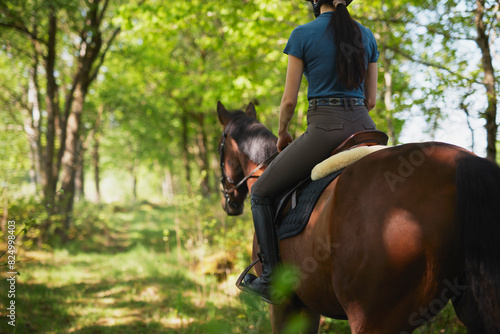 Low section of female trainer riding horse towards green trees photo