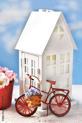 Home decor with red metal bike standing in front of miniature house
