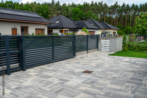 A modern panel fence in anthracite color, visible sliding gate to the garage and a garbage place in the corner.