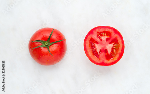 Tomato with half of tomato on a white marble background, top view