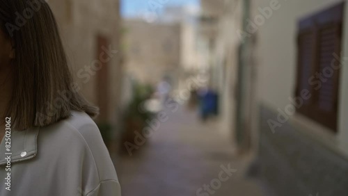 A young hispanic woman confidently walks through the charming stone streets of polignano a mare in puglia, italy, enjoying a beautiful day. photo