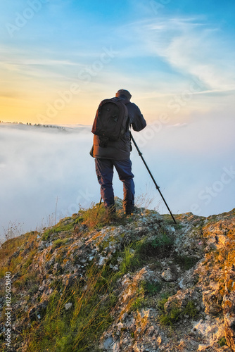 Autumn morning. Traveler on the top of rock above river valley with thick fog. Nature of Ukraine