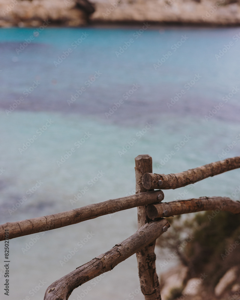 Turquoise waters of Menorca's coves, framed by a typical wooden railing, set in the stunning Balearic Islands landscape.
