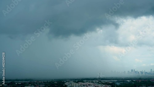 Dark clouds release tropical heavy downpour over cityscape, signaling sudden rainstorm. photo