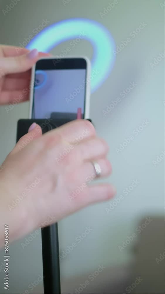 Close-up of hands setting up phone for vlog at home, photographer adjusting equipment, phone on tripod with ring light in background. Close-up of hands setting up phone for vlog at home, photographer adjusting equipment, phone on tripod with ring light in background.