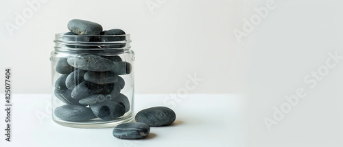 Black rocks artistically arranged in a clear glass jar, set on a white background to emphasize contrast photo