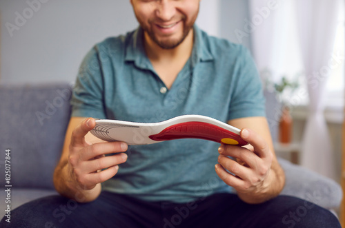 Positive man is sitting on the sofa, inspecting an orthopedic insole. Hands holding the insole, emphasizing health and medical care for feet. Perfect for orthopedics related concepts. photo