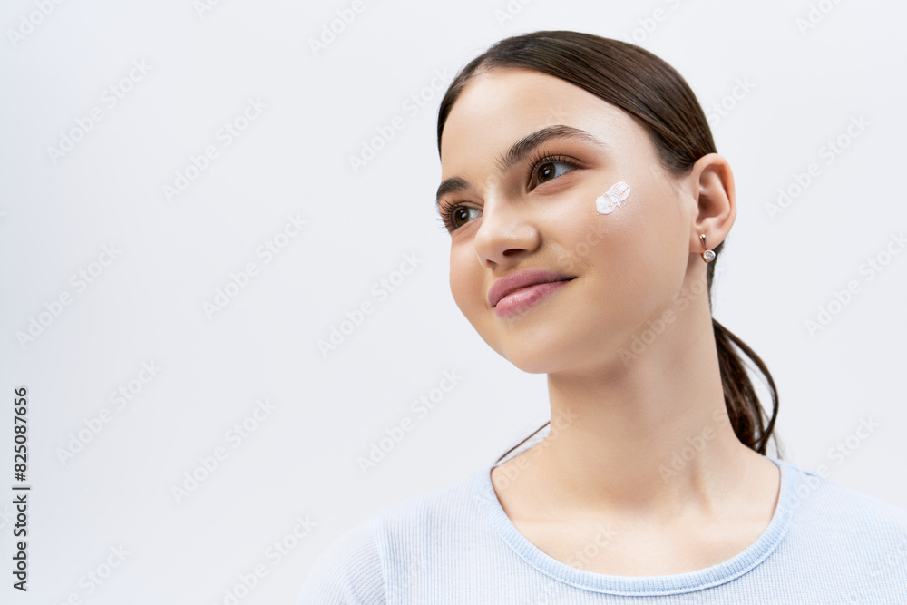 A gorgeous brunette teenage girl applying white face cream to her cheek, exuding youthful beauty. A gorgeous brunette teenage girl applying white face cream to her cheek, exuding youthful beauty.