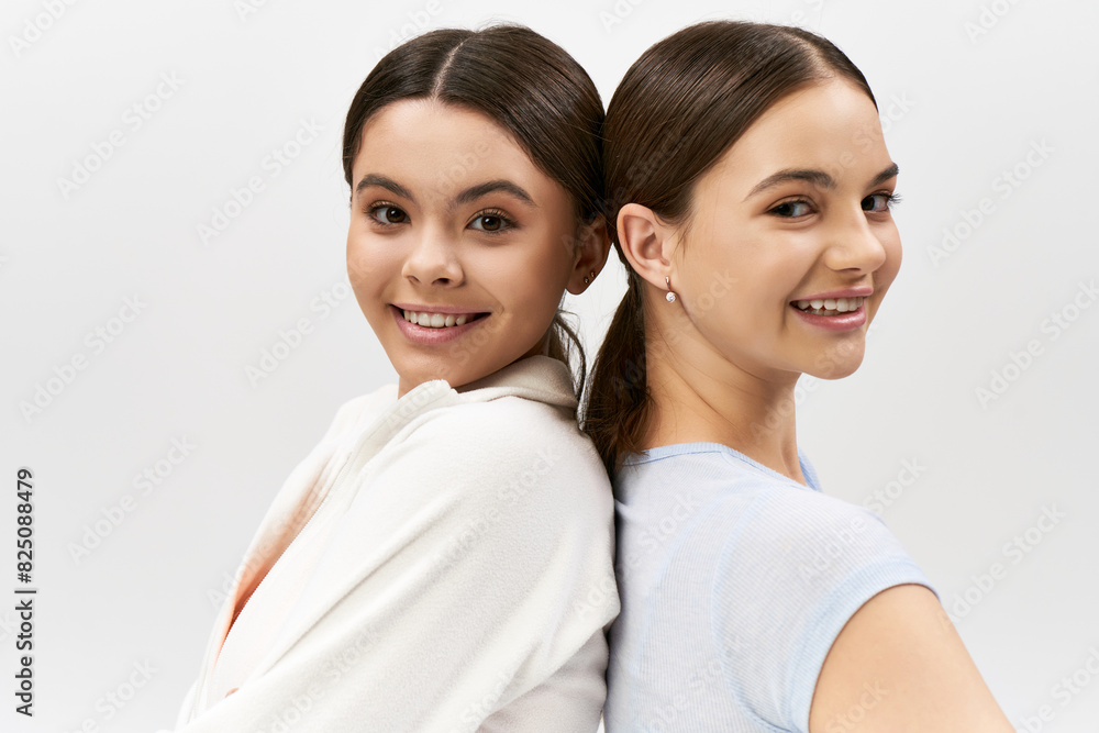 Two pretty brunette teenage girls in sportive attire standing side by side in a studio setting. Two pretty brunette teenage girls in sportive attire standing side by side in a studio setting.