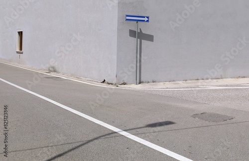 Directional arrow traffic sign on a pole at corner street with gray plaster wall on behind. Urban street in front. Background for copy space.