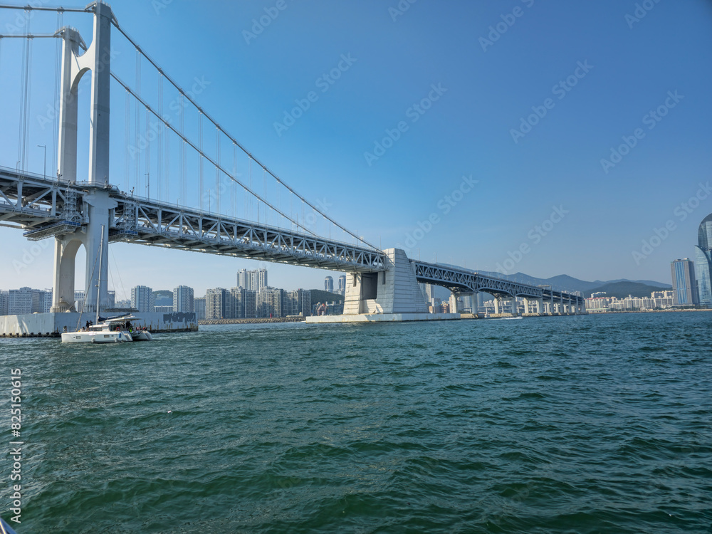 Naklejka premium A large bridge spans a body of water, with a boat in the foreground. The bridge is a modern structure, and the water is calm and clear. Concept of tranquility and peacefulness, as the bridge