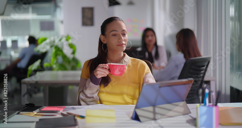 Indian Asian Hindu young adult busy girl woman lady staff sitting chair office use tablet touch pad task day gen z female expert worker hold cup drink hot warm coffee tea enjoy break time at job place photo