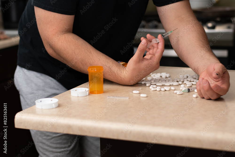 Man trying to inject a sustance with a syringe and a table full of drugs Man trying to inject a sustance with a syringe and a table full of drugs