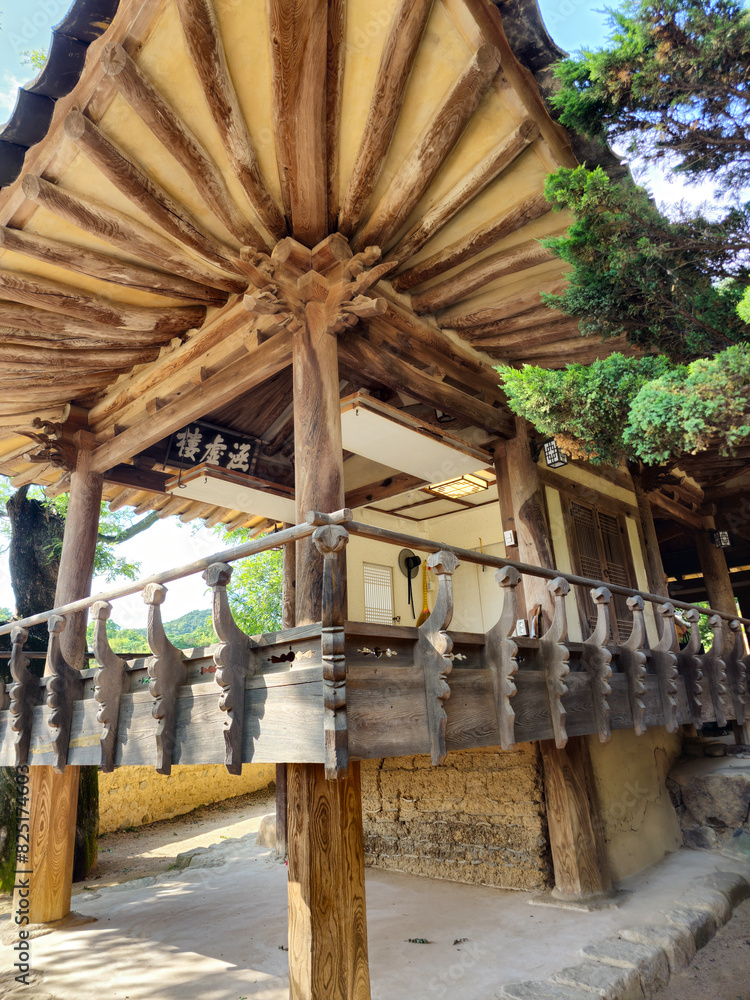 Fototapeta premium A small wooden building with a balcony and a roof. The roof is made of wood and has a slanted design. The building is surrounded by trees