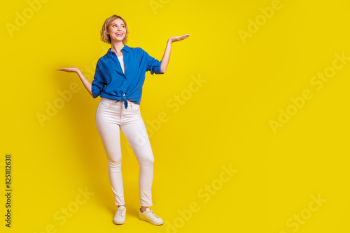 Full size portrait of pretty young lady hold show empty space wear shirt isolated on yellow color background