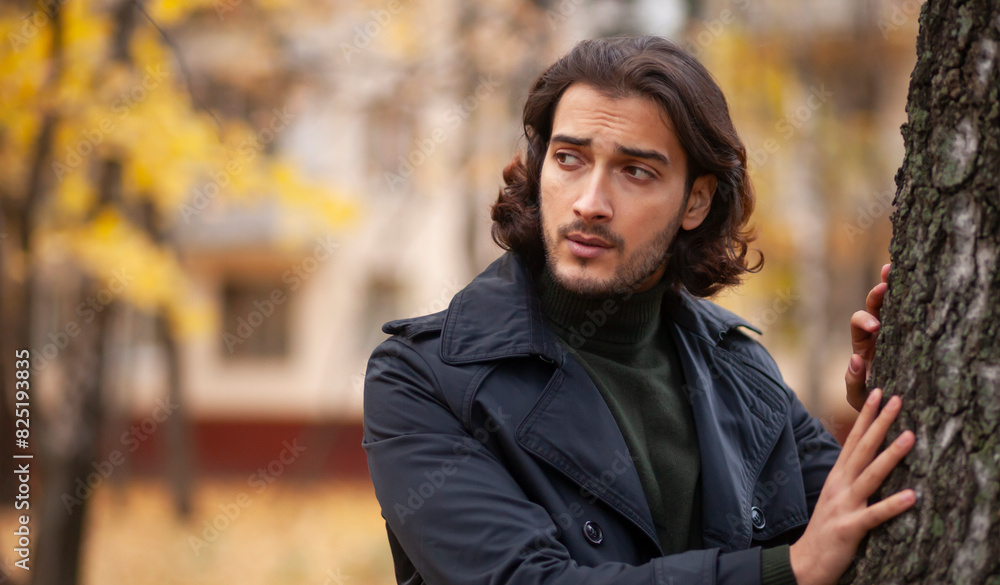 Portrait of handsome long haired man in black trench coat in the park in wonderful autumn day. Fashion and style concept Portrait of handsome long haired man in black trench coat in the park in wonderful autumn day. Fashion and style concept