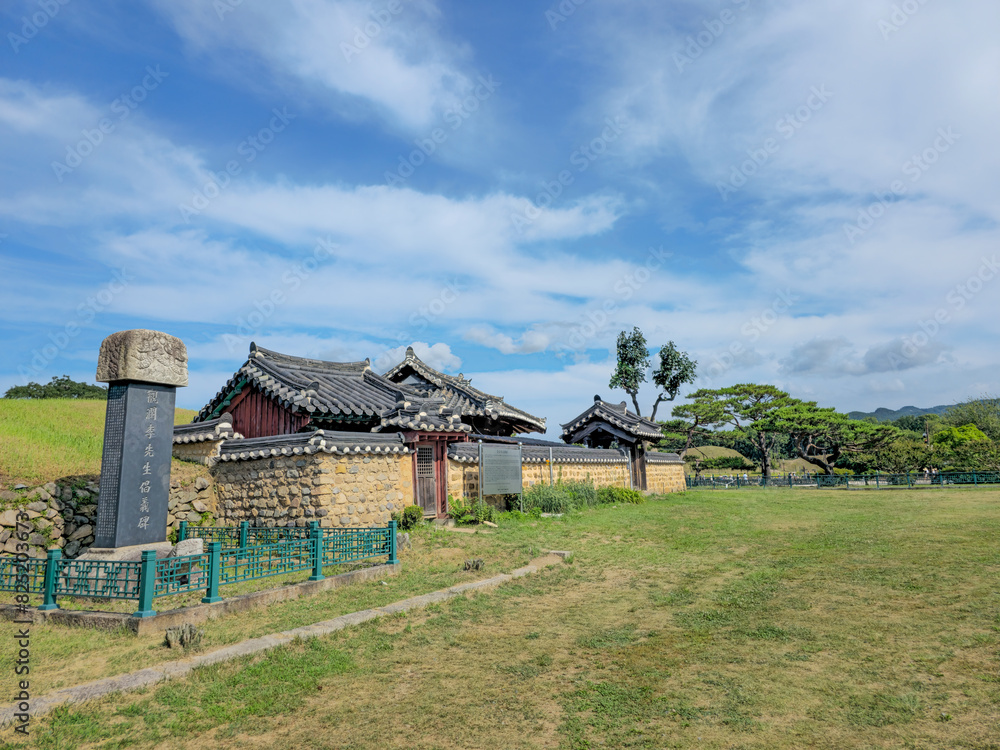 A small house with a fence and a sign in front of it. The house is surrounded by a field and trees A small house with a fence and a sign in front of it. The house is surrounded by a field and trees