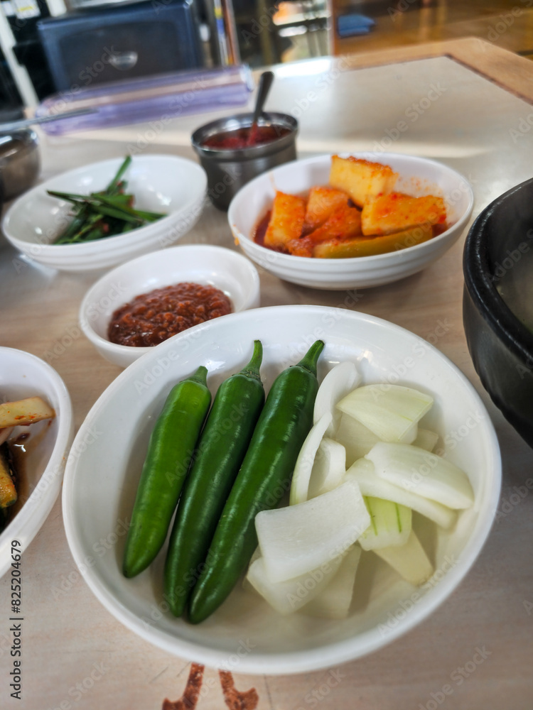 A table with several bowls of food, including one with green peppers and onions. The table is set for a meal, and the food looks fresh and appetizing A table with several bowls of food, including one with green peppers and onions. The table is set for a meal, and the food looks fresh and appetizing