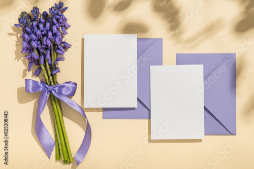 A bouquet of lavender spring Scilla, two lilac envelopes and blank cards on a beige background. Greeting card.