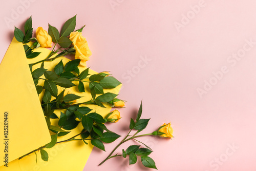 Invitation or greeting card mockup with yellow envelope with small yellow roses on pink background.Copy space.