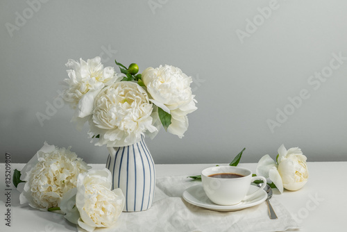 Morning cup of coffee and white peonies in a vase on the table. Summer mood. Copy space.
